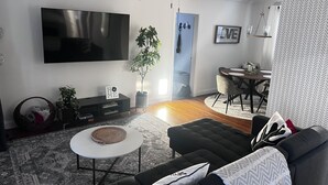 A modern living room with a flat-screen TV, a dark sofa, a round coffee table, and a dining area with a table and chairs. - This place is peaceful  to stay in, Relax and enjoy. (Greenville)