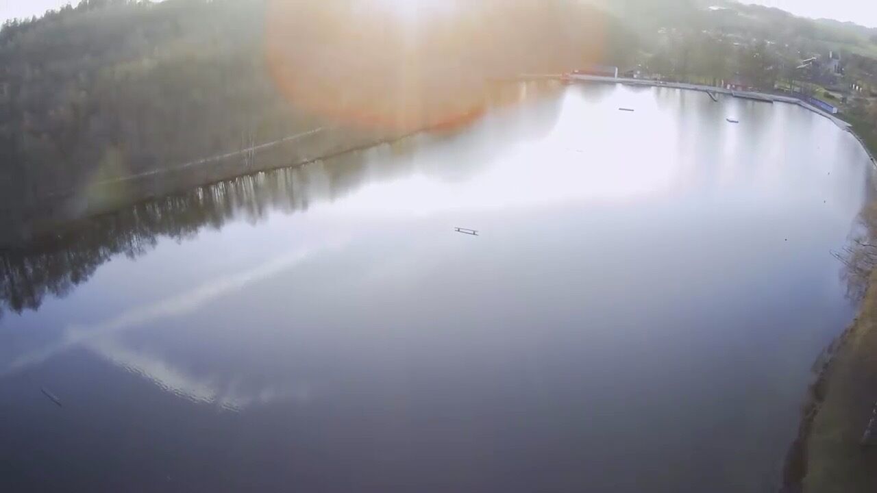 A calm lake with a bridge and forested hills in the background.