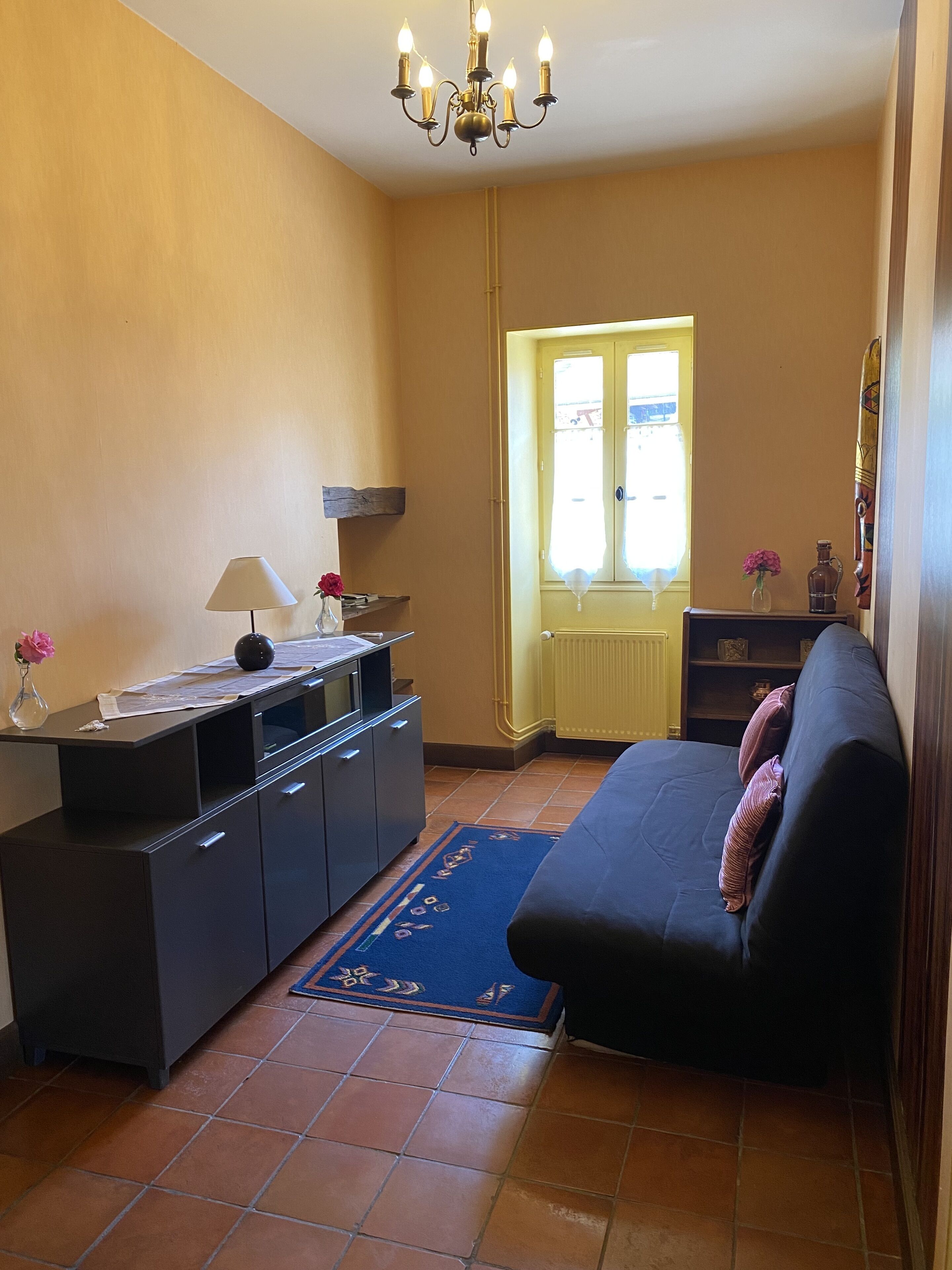 Un salon comprenant un canapé, un meuble, une lampe, un vase avec des fleurs et une fenêtre donnant sur un beau paysage.