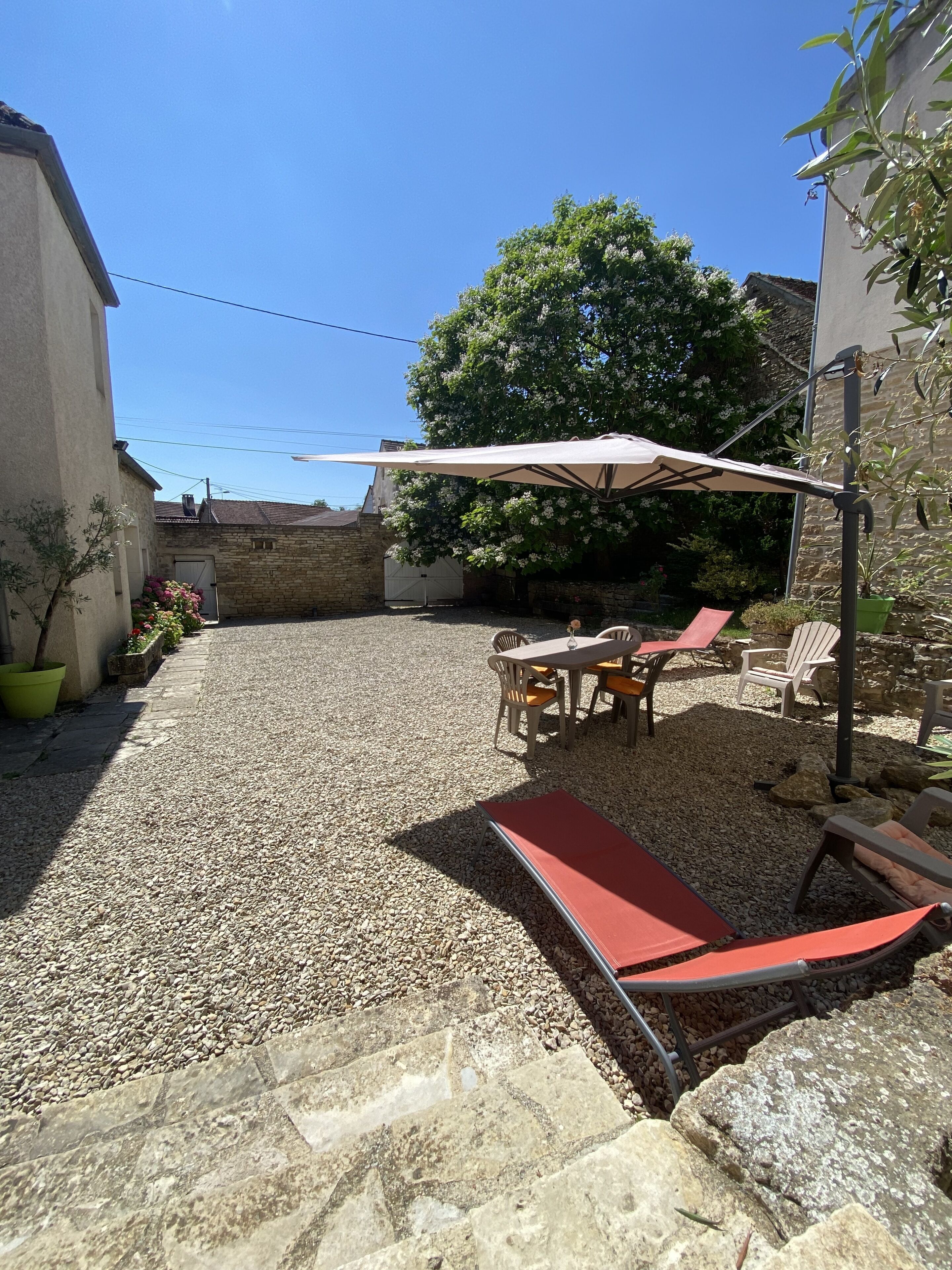 Un patio con mesa y sillas bajo un paraguas grande, rodeado de grava y plantas en macetas.