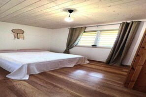 Quarto com cama, piso de madeira, ventilador de teto, janela com cortinas e um adorno na parede.