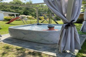 Un jacuzzi dans un jardin, avec un toboggan et des jeux pour enfants en arrière-plan.