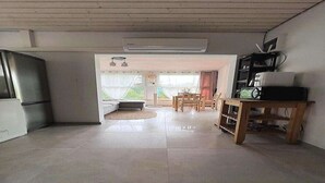 A spacious living area with a large window, a dining table, and a kitchen area with a refrigerator. - Holiday Home near Baltic Sea & Golf Course (Kołczewo)