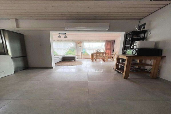 A spacious living area with a large window, a dining table, and a kitchen area with a refrigerator. - Holiday Home near Baltic Sea & Golf Course (Kołczewo)