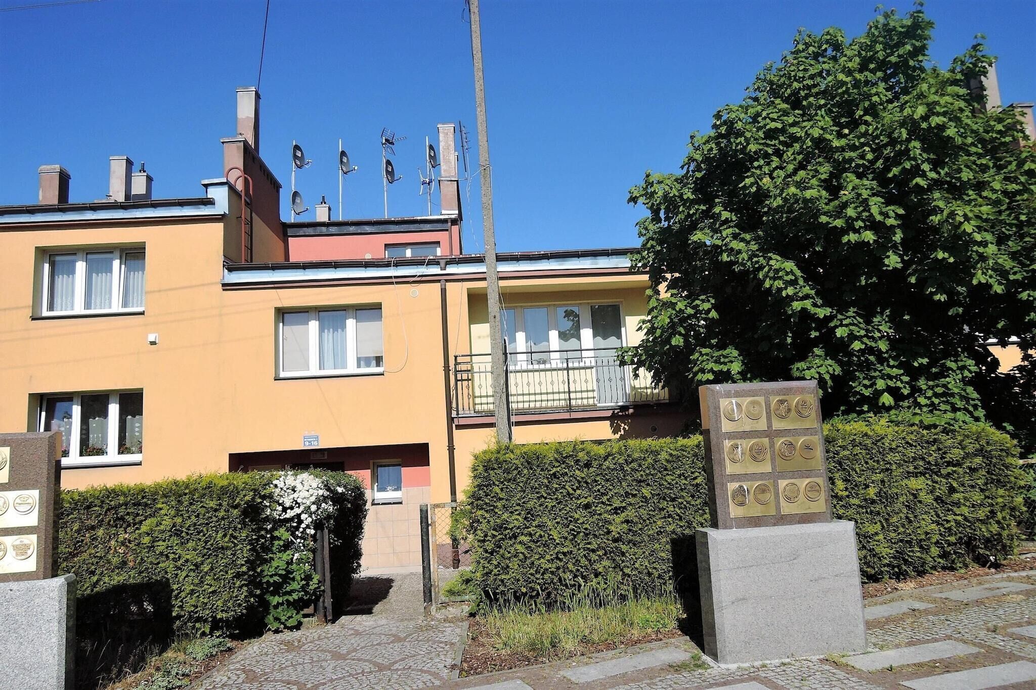 A yellow building with multiple windows and a balcony. There are two plaques in front of the building.