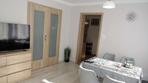 Un soggiorno moderno con una TV a schermo piatto, mobili contenitori in legno, un tavolo da pranzo con sedie e una lampada a sospensione.
