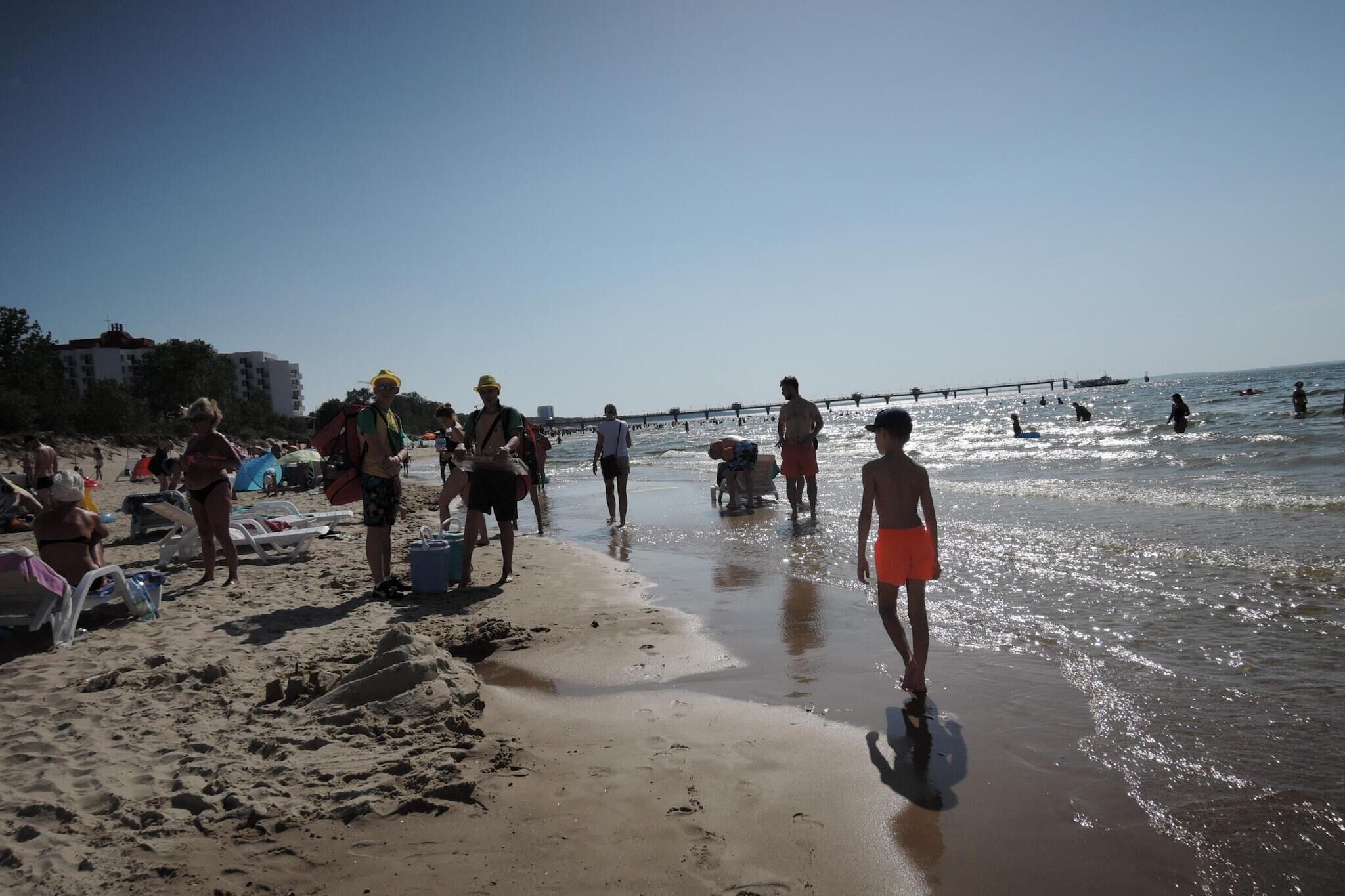 A beach with people walking and standing in the sand, some near the water's edge.