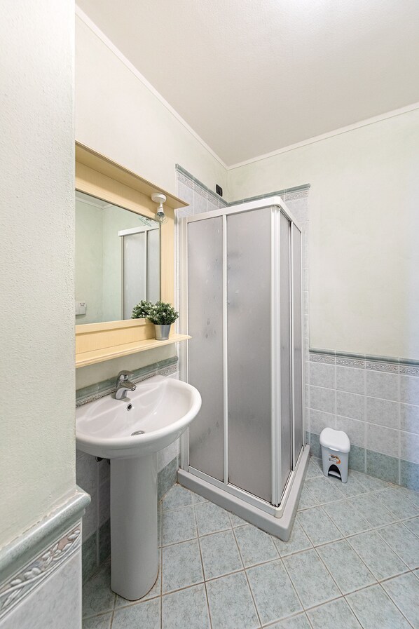 A bathroom with a sink, mirror, shower enclosure, and a small trash bin. - I Mosaici Apartment by Wonderful Italy (Sirmione)
