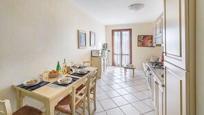 Ein Essbereich mit einem Tisch für zwei Personen, eine Küche mit weißen Schränken und ein Fenster mit Vorhängen.