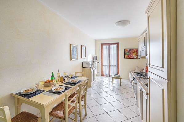 Comedor con mesa dispuesta para dos, cocina con armarios blancos y ventana con cortinas.