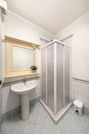 A bathroom with a pedestal sink, a mirror, a shower enclosure, and a small trash bin. - I Mosaici Apartment by Wonderful Italy (Sirmione)