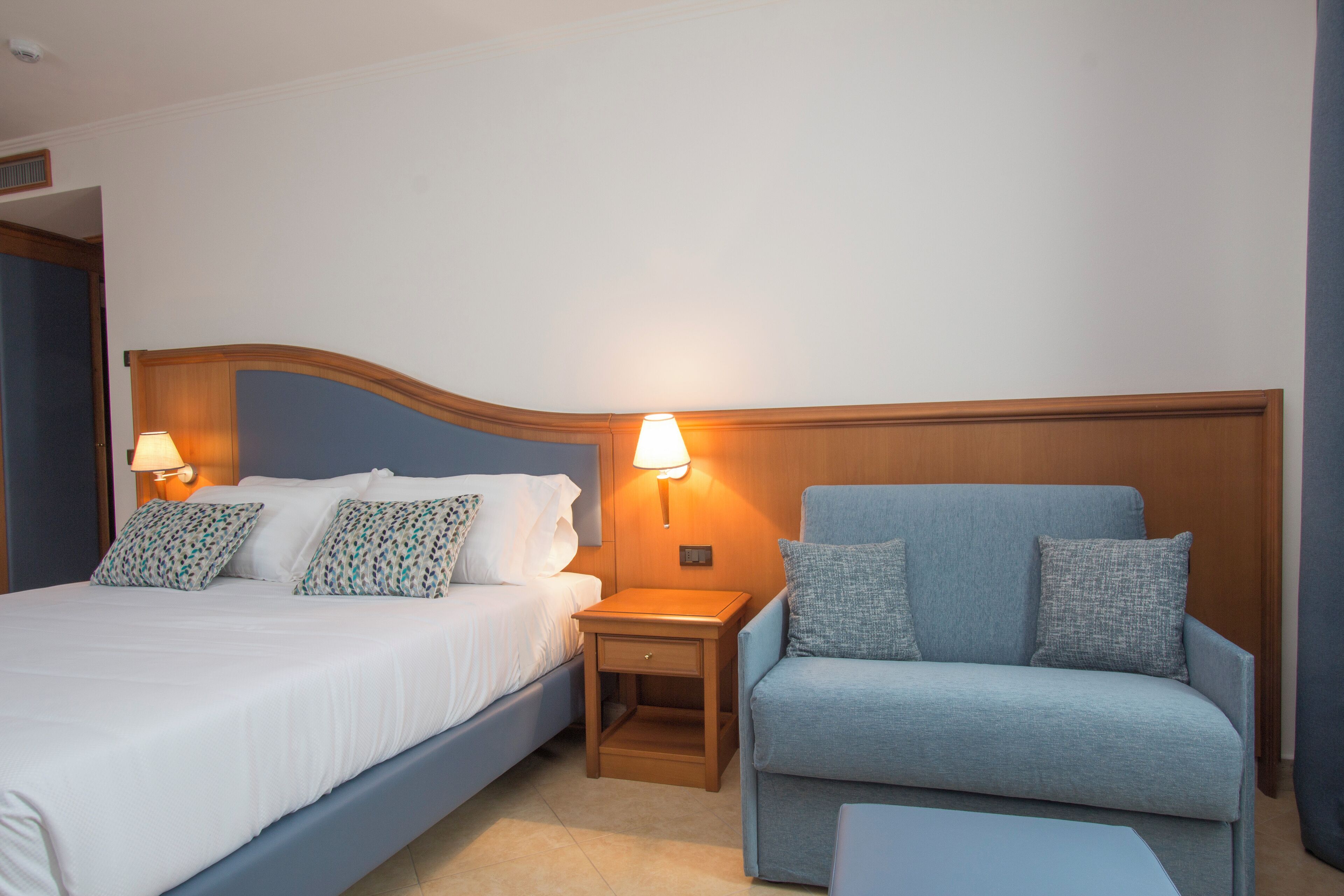 Ein Hotelzimmer mit einem Bett, einem Nachttisch mit Lampe und einem blauen Sessel.