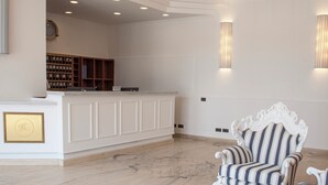 A reception area with a white reception desk, a striped armchair, and a wall-mounted clock. - Hotel Centrale (Sabaudia)