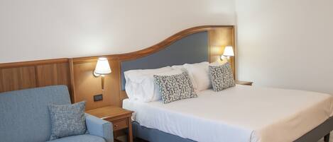 A bedroom with a bed, a nightstand, a lamp, a sofa, and a patterned pillow.