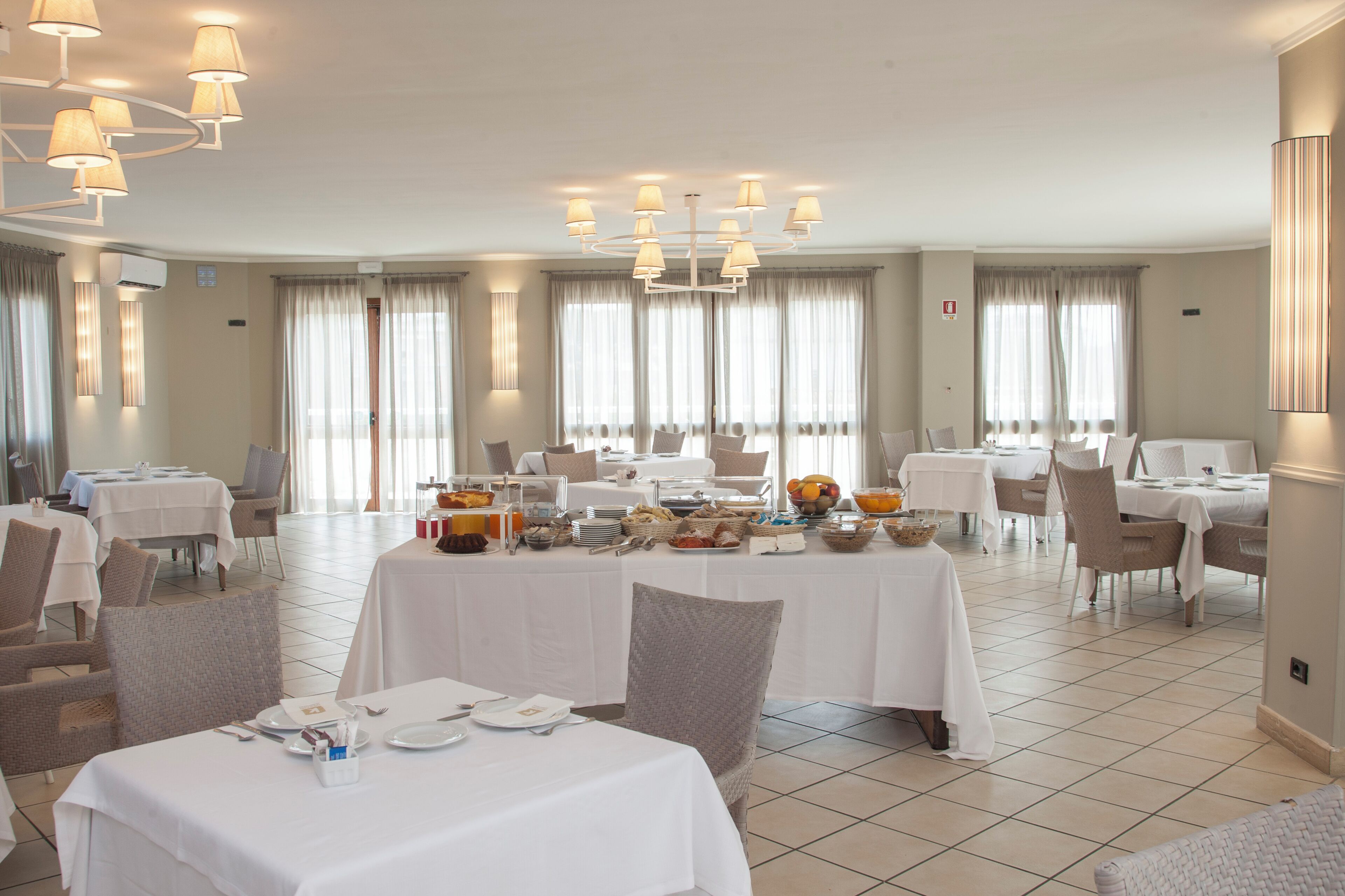 Un'ampia sala da pranzo con diversi tavoli apparecchiati per la colazione, con una varietà di pietanze e un moderno lampadario.