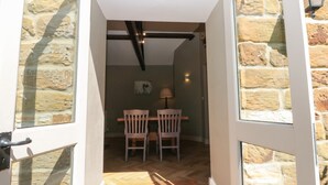 Una porta oberta que dona a una habitació amb taula i cadires de fusta, una làmpada i una paret de pedra.