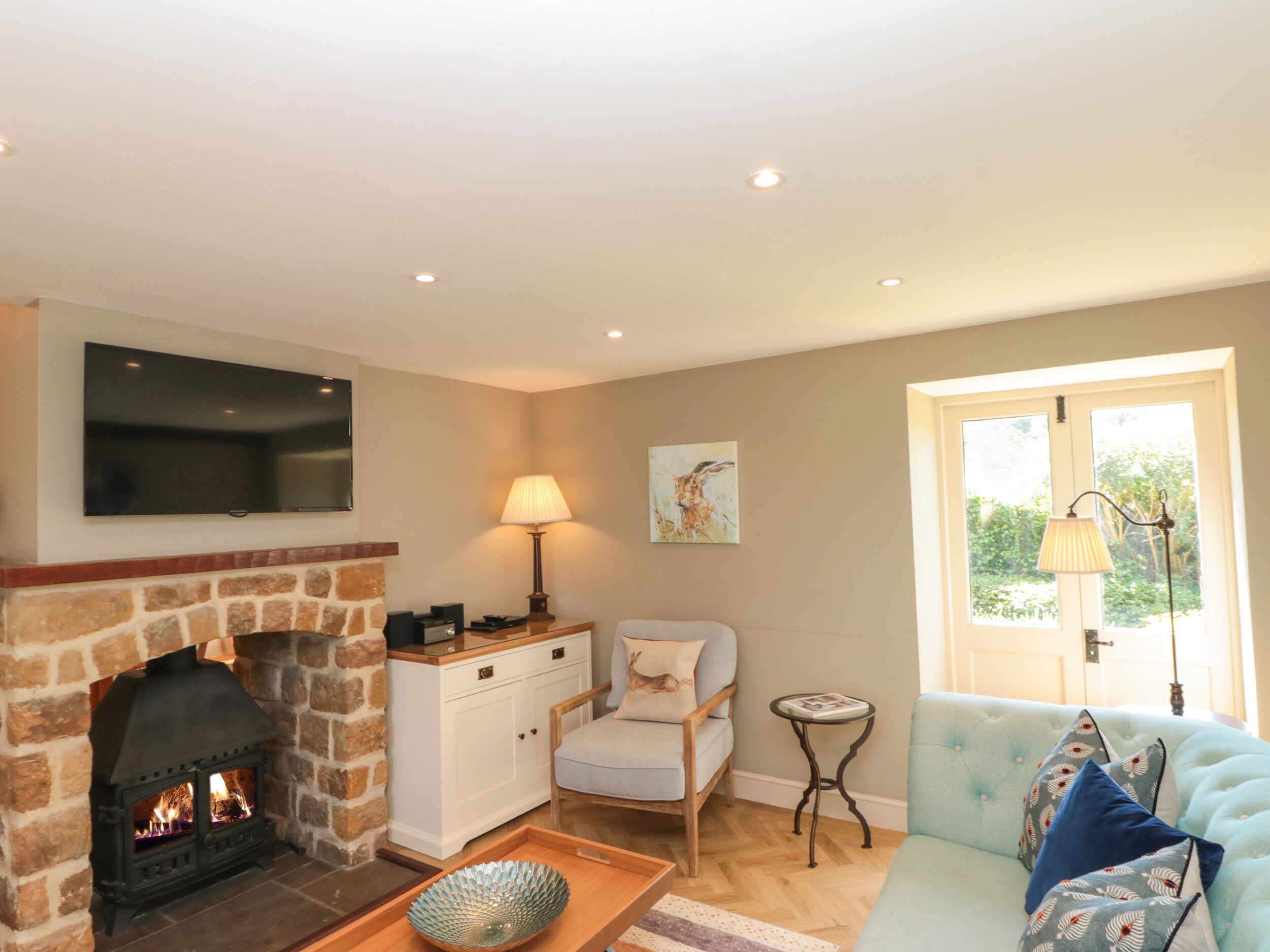 A cozy living room with a stone fireplace, a television mounted on the wall, a comfortable sofa, and a small side table.