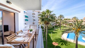 Een balkon met een eettafel gedekt voor twee personen, met uitzicht op een zwembad en palmbomen.