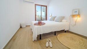 Een slaapkamer met een bed, een raam, een wandlamp, een luchtverkoeler en een geweven vloerkleed.