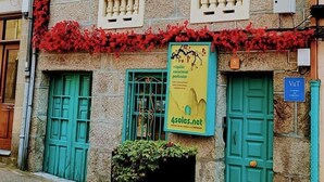Un edificio de dos pisos con contraventanas verdes, un balcón con barandilla de metal ornamentada y un cartel que anuncia un alquiler vacacional.