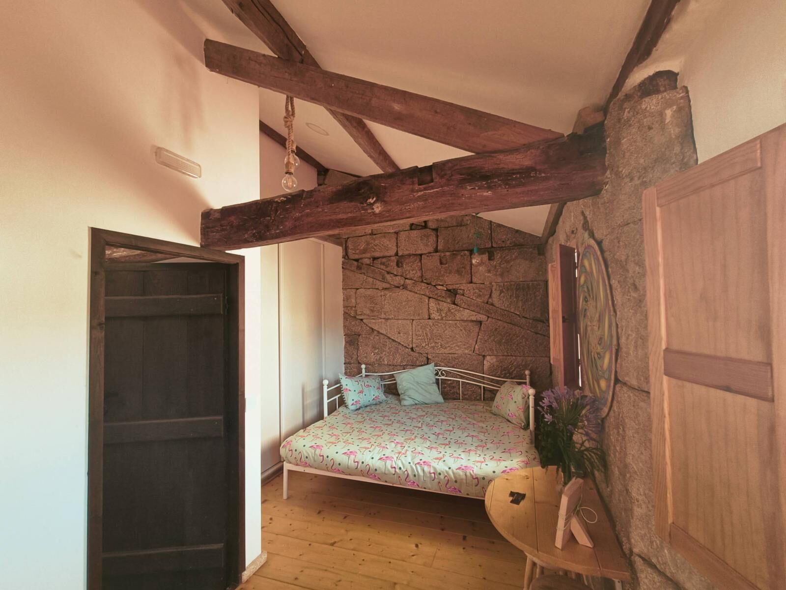 A bedroom with a bed, wooden beams, stone wall, and a door.