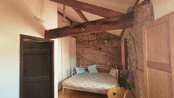 A bedroom with a bed, wooden beams, stone wall, and a door.