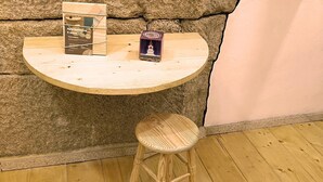 Un taburete de madera y una mesa pequeña con una caja y una tarjeta encima, frente a una pared de piedra.