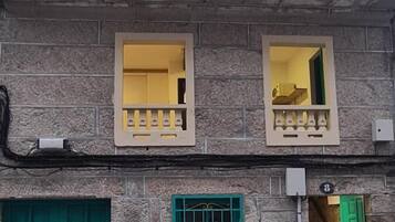Un edificio de dos pisos con fachada de piedra, puertas verdes y un pequeño balcón con barandilla decorativa.