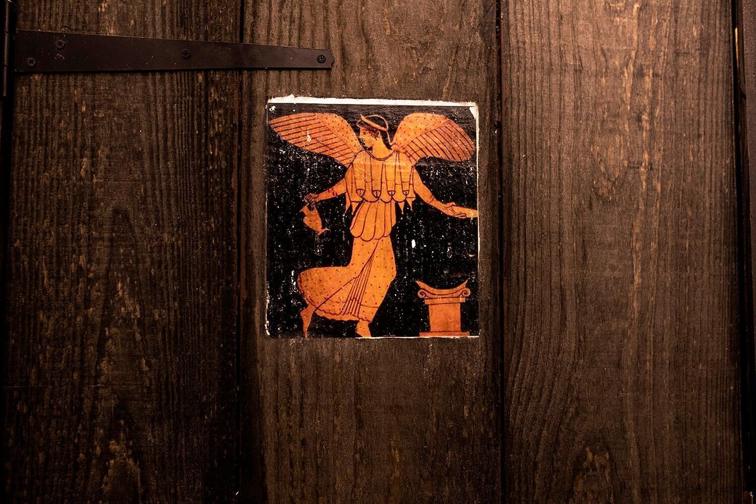 Une porte en bois sur laquelle est fixée une petite plaque usée représentant une figure angélique.
