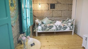 A cozy room with a bed, a small round table with a vase, and a stone wall. - Dea Dana Studio Ponte Caldelas (Ponte Caldelas)