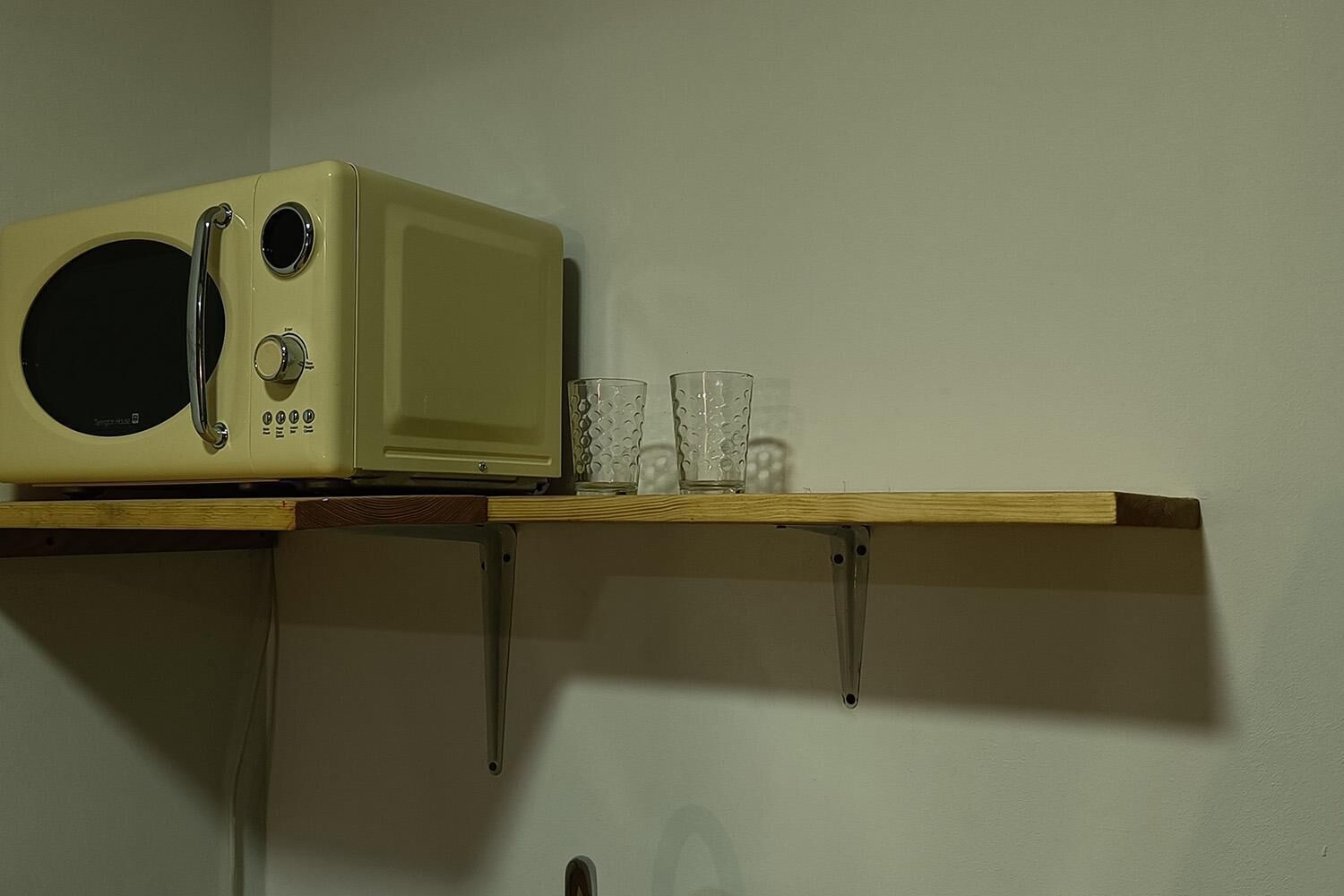Un microondas sobre una repisa de madera, con vasos abajo.