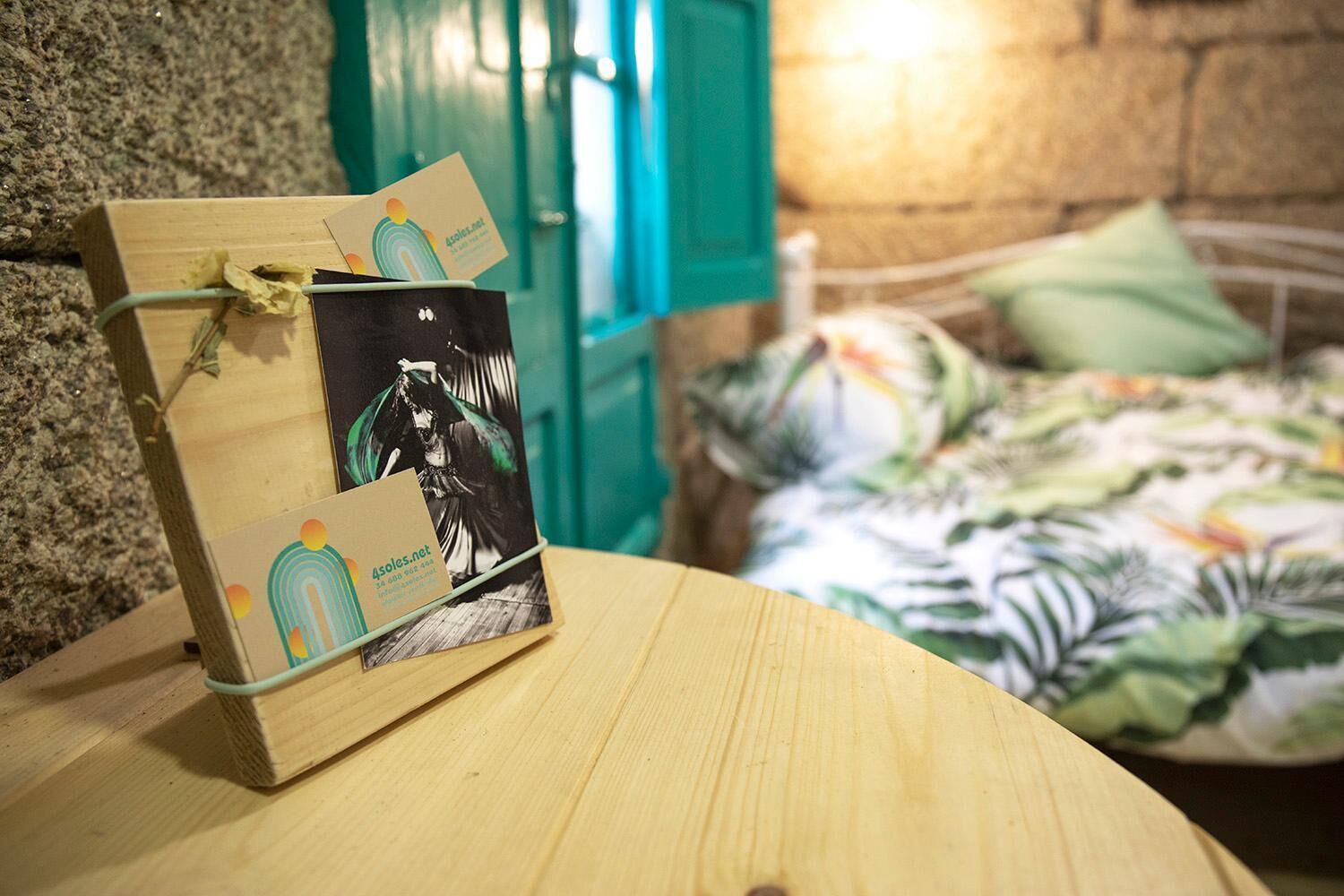 Een houten doosje met een visitekaartje eraan, geplaatst op een houten ondergrond in een kamer met een bed en een groene deur.