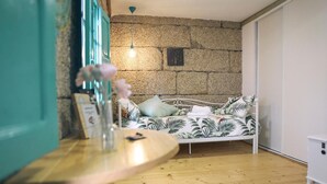 A room with a bed against a stone wall, a small table with a vase, and a wooden floor. - Dea Dana Studio Ponte Caldelas (Ponte Caldelas)