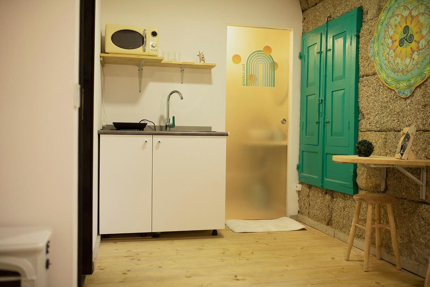 A compact kitchen with white cabinets, a microwave, and a sink. There's a small stool and a table with a decorative item.
