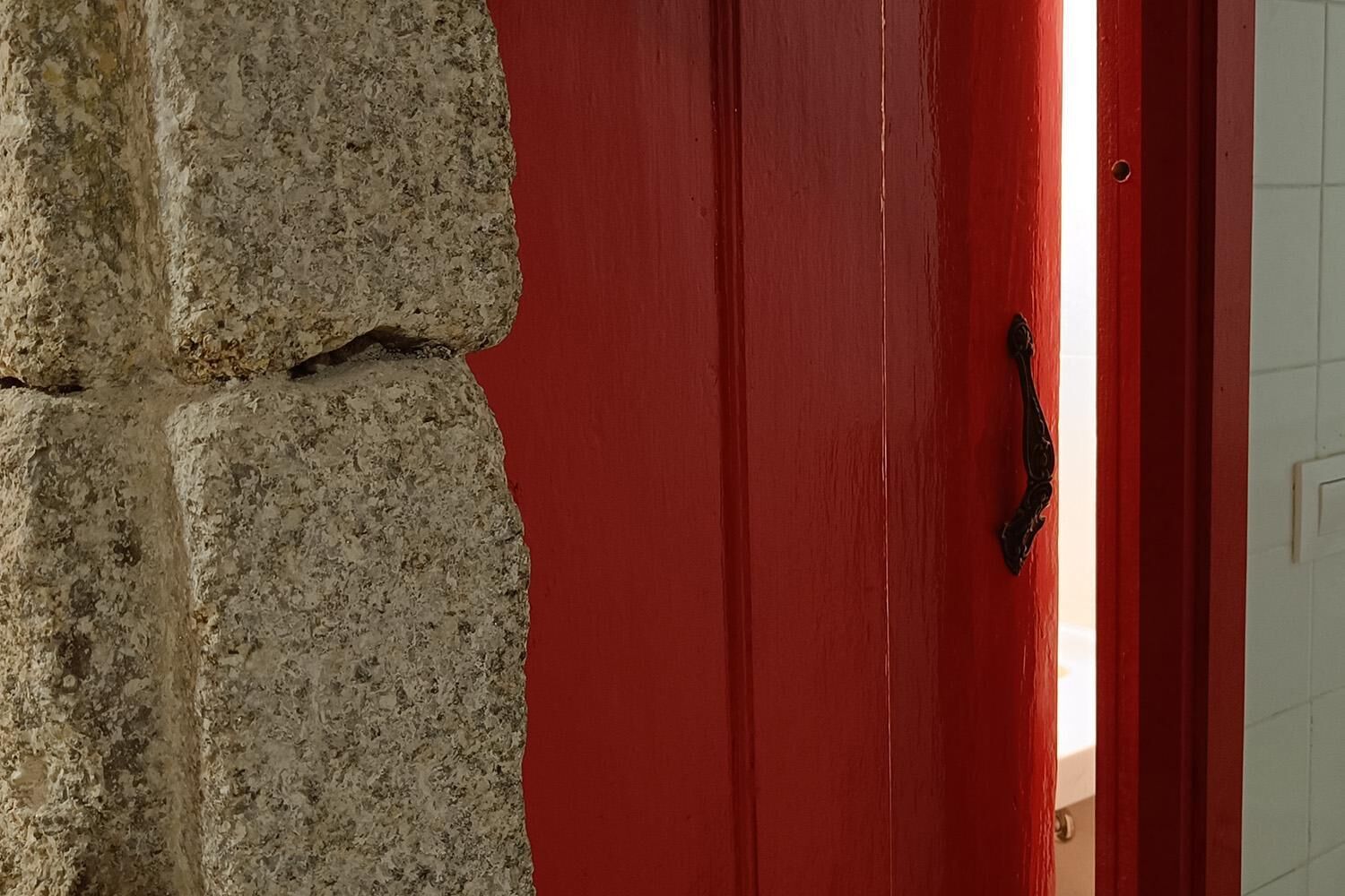 A red door with a black handle, adjacent to a textured stone wall.
