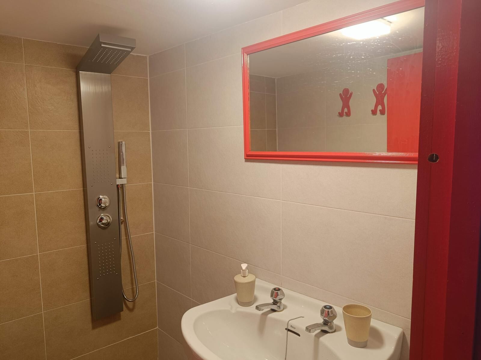 Une salle de bain avec une douche, un lavabo et un miroir doté d’un cadre rouge.