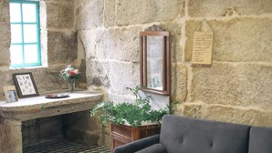 Una habitación con paredes de piedra, una ventana, un escritorio con un florero, un cuadro enmarcado y un espejo.