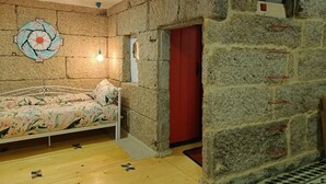 Una habitación con una cama, una pared de piedra y una puerta roja.