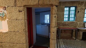 Una habitación con paredes de piedra, piso de madera y ventana con contraventanas azules.