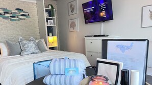A hotel room with a bed, a bedside table with a candle, a remote control, and a framed welcome sign.