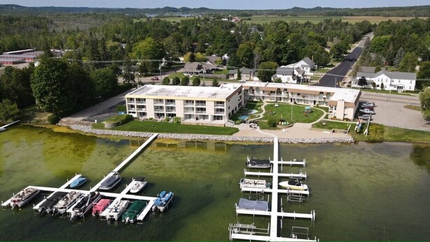 An aerial view of a hotel with a dock and boats, surrounded by greenery and a road.