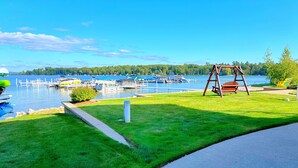 A grassy area with a swing set and a dock with boats in the background.