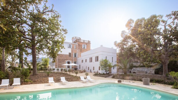 A swimming pool with lounge chairs, surrounded by trees and a building with a white facade and arched windows. - La Bâtisse en Blanc (Vallauris)