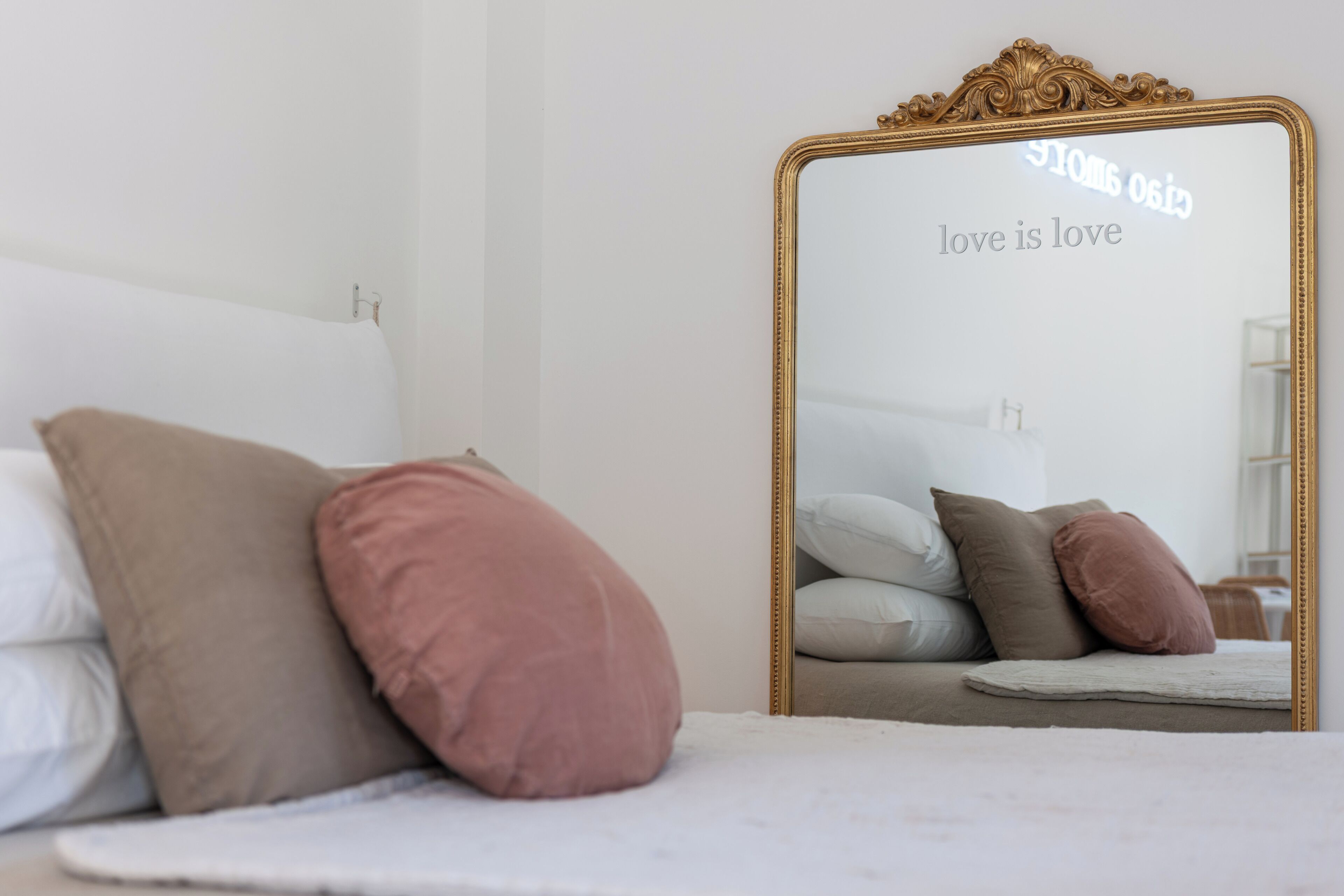 A bedroom with a bed, pillows, and a mirror with a gold frame.