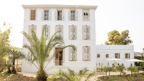 A white building with multiple windows and shutters, surrounded by greenery and outdoor seating. - La Bâtisse en Blanc (Vallauris)