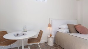 A room with a bed, a table, wicker chairs, a bedside lamp, and a neon sign. - La Bâtisse en Blanc (Vallauris)