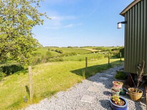 A rural landscape with a gravel path leading to a wooden structure, surrounded by greenery and sheep grazing. - Puddle Duck Shepherds Hut (Launceston)