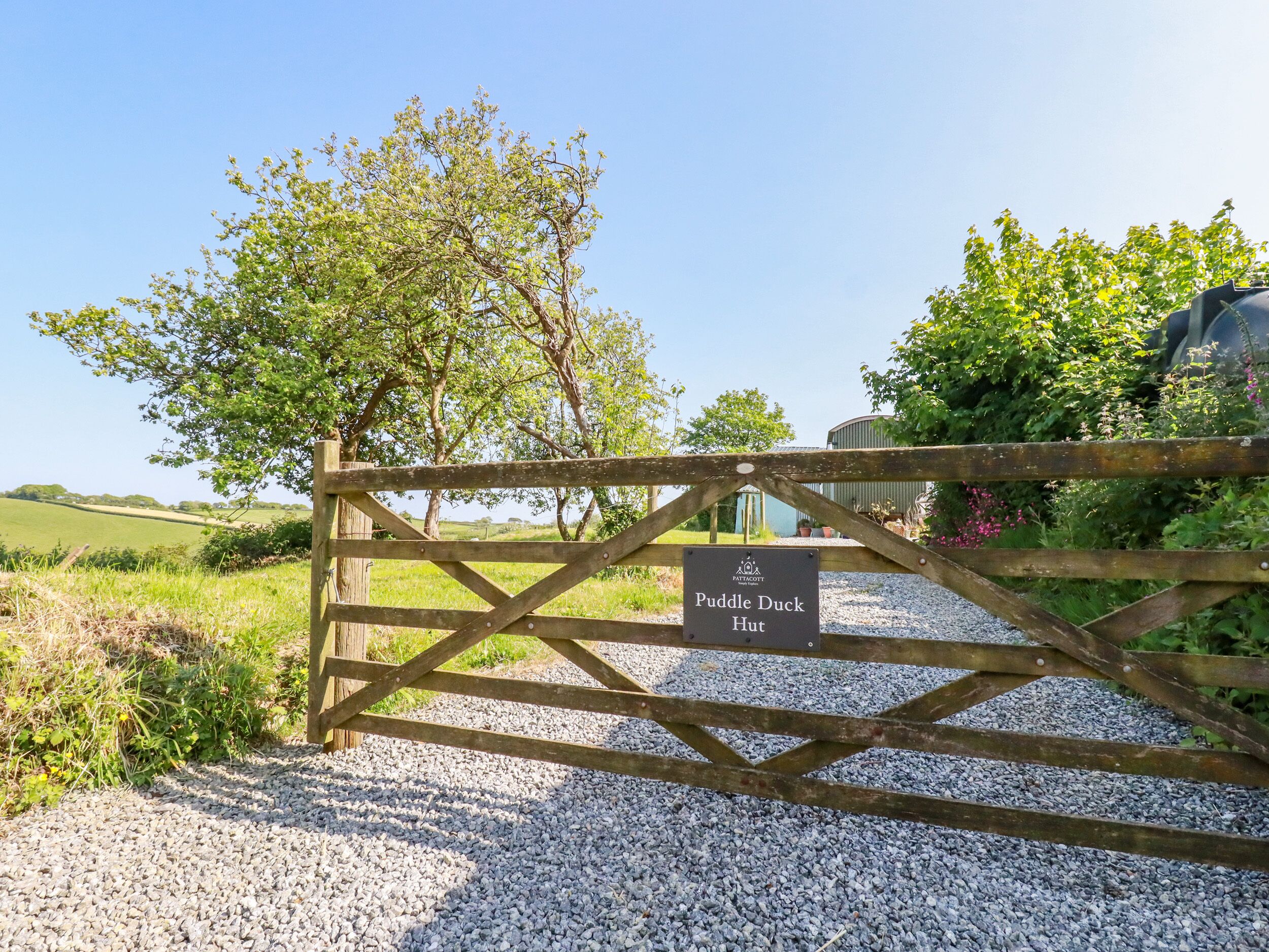 A gravel path leading to a wooden gate with a sign reading 'Puddle Duck Hut.'
