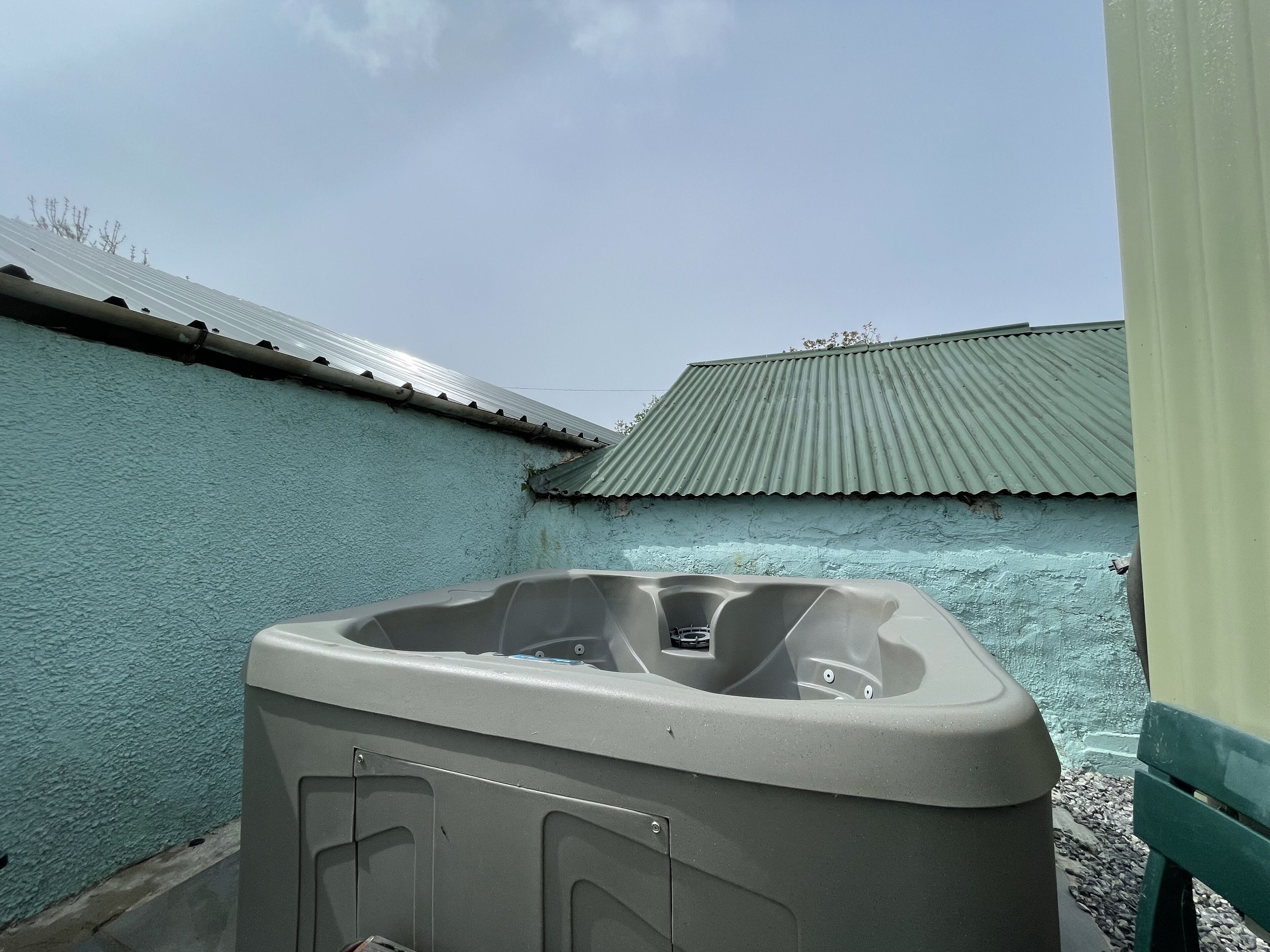 A hot tub in an outdoor area with a blue wall and a green roof.