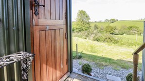 Una porta in legno con maniglia e serratura in metallo, che dà su un balcone con vista su un campo verde e alberi.